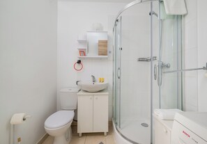 Un bany modern amb dutxa envidriada, vàter i un lavabo amb armari.