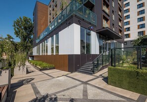 Een modern gebouw met een glazen gevel, een houten terras en een trap die naar een hoger niveau leidt.