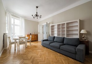 Een ruime woonkamer met een visgraatparketvloer, een grijze bank, een eettafel met stoelen en een witte kast.