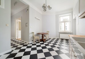 A room with a checkered floor, a round table with chairs, a chandelier, and a window with blinds. - Poznańska City Center Soul Apartment (Warszawa)