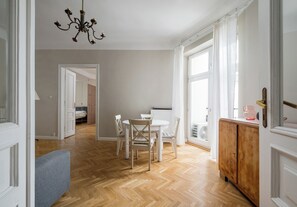 A spacious room with a wooden herringbone floor, a dining area with white chairs, a wooden cabinet, and a chandelier. - Poznańska City Center Soul Apartment (Warszawa)