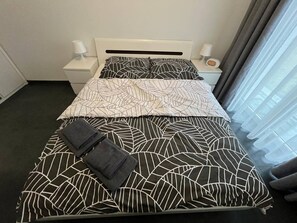 Et hotelværelse med en seng, to sengeborde og et vindue med gardiner.