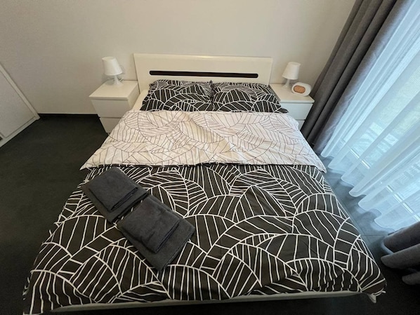 A hotel room with a bed, two bedside tables, and a window with curtains.