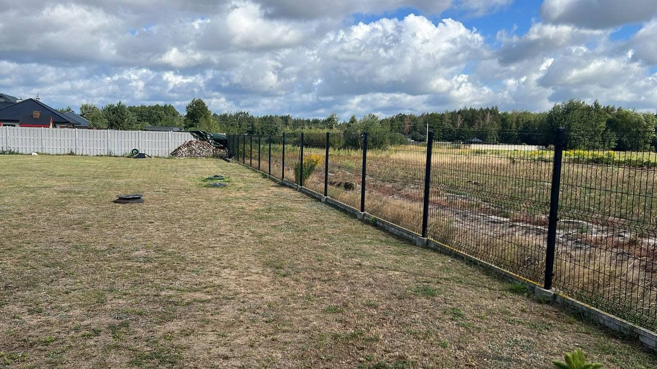 A fenced outdoor area with a grassy field and a pile of firewood.