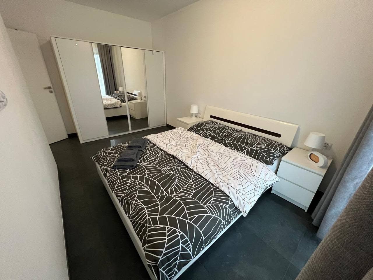 A modern hotel room with a bed, bedside tables, a mirror, and a wardrobe.
