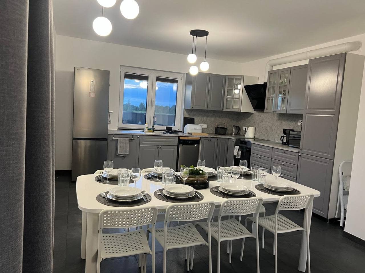 Una cucina moderna con un tavolo da pranzo per sei persone, dotata di elettrodomestici in acciaio inossidabile, mobili in color grigio e illuminazione a sospensione.