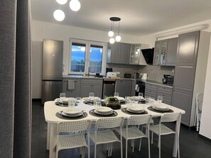 A modern kitchen with a dining table set for six, equipped with stainless steel appliances, grey cabinetry, and pendant lighting. - Stodoła Kuczki Wieś Cottage (Kuczki-Wieś)