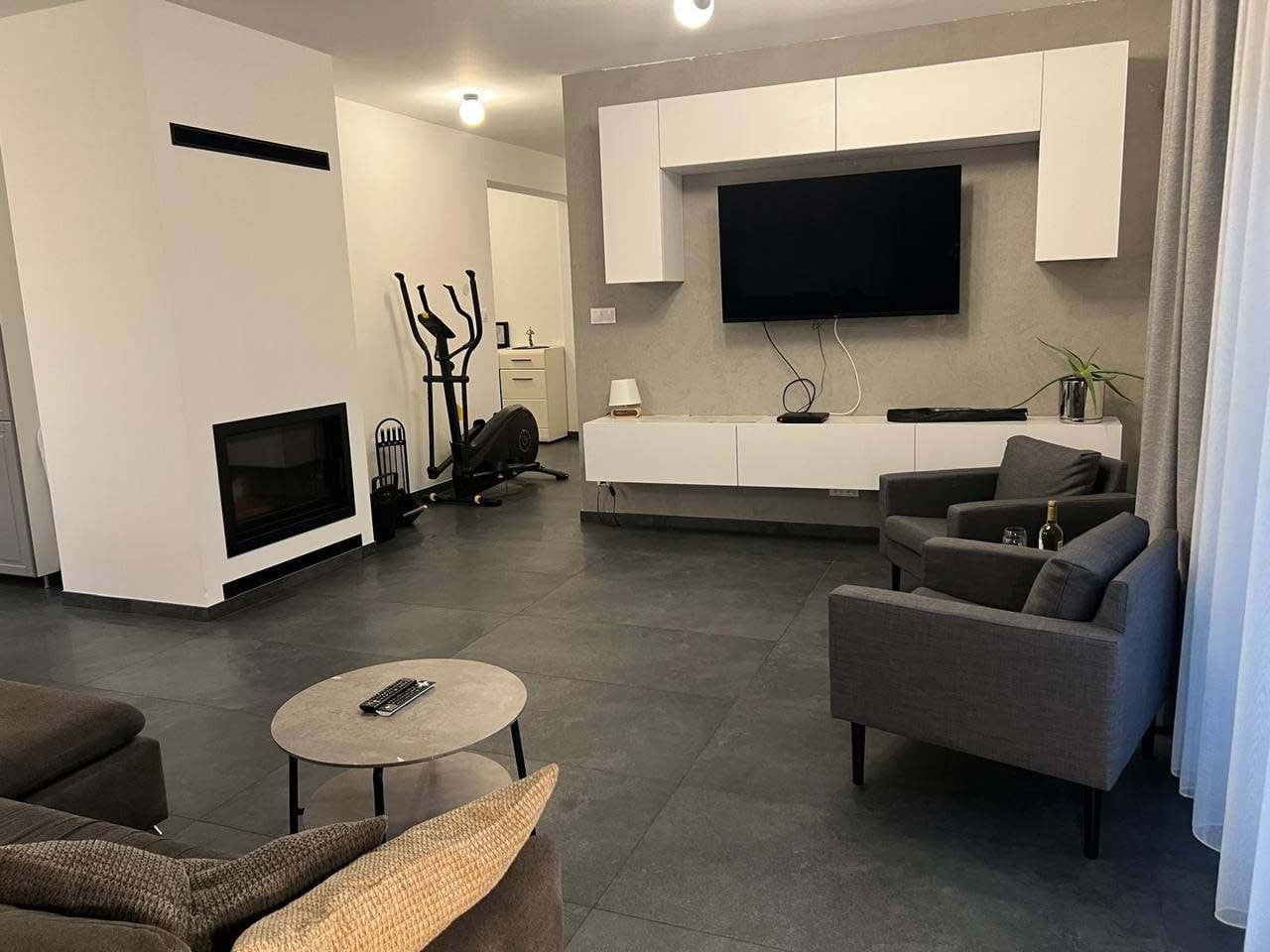 A modern living room with a fireplace, sofa, coffee table, and a flat-screen TV mounted on the wall.