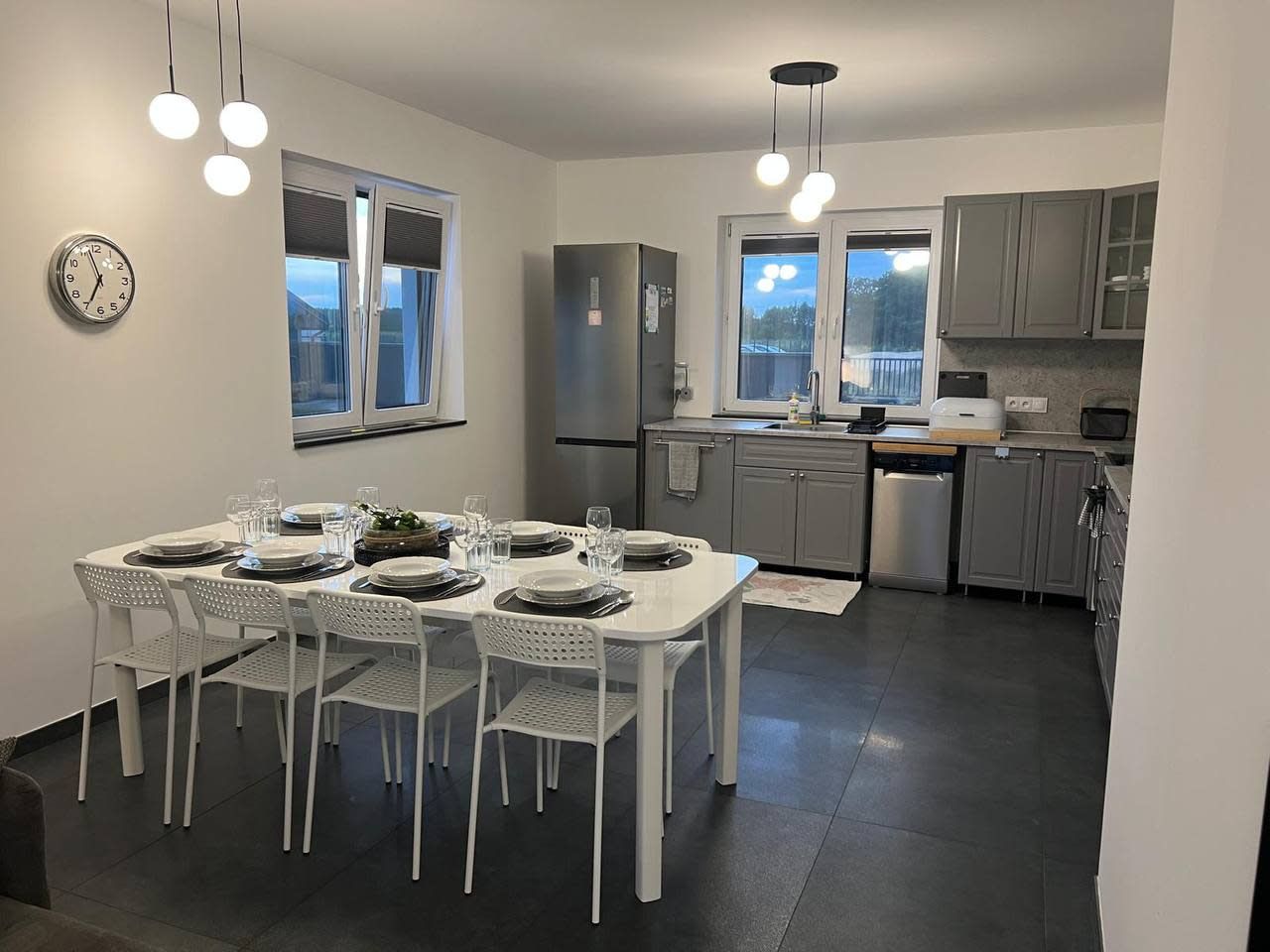 Una cocina moderna con armarios blancos, horno empotrado y comedor con mesa blanca para cuatro.
