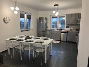 Una cocina moderna con armarios blancos, horno empotrado y comedor con mesa blanca para cuatro.