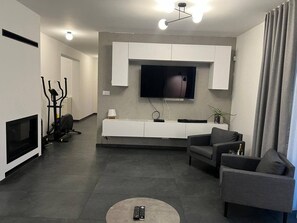 En moderne stue med et fladskærms-tv, grå sofaer, et hvidt konsolbord og en pejs.