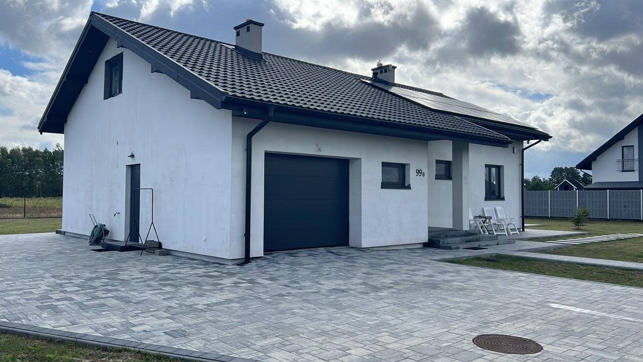 A modern two-story house with a garage, a paved driveway, and a small garden area.