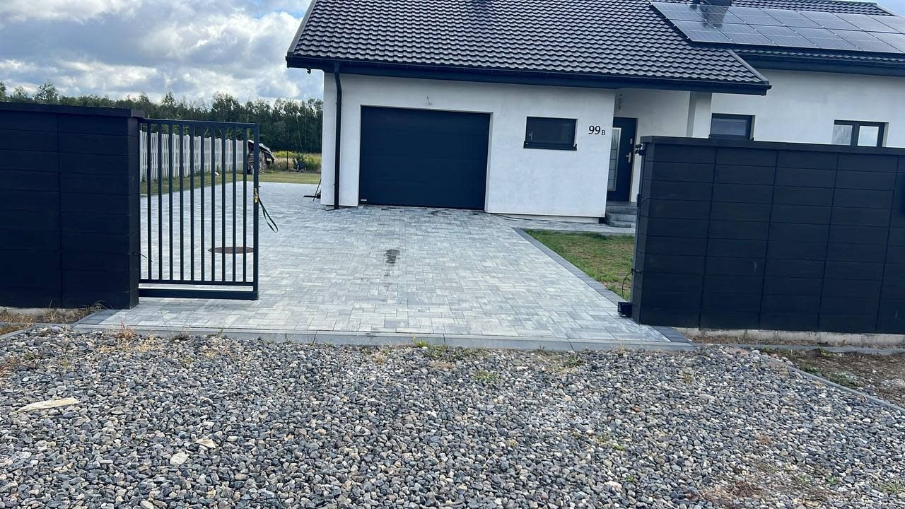 A modern house with a garage, a gated driveway, and a gravel front yard.