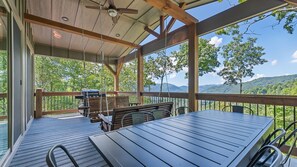 A covered outdoor deck with a table and chairs, overlooking a mountainous landscape. - The Courtside Suites at Beatitude Barn (Maggie Valley)
