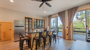 A modern kitchen with a central island, bar stools, and a view of the outdoors. - The Courtside Suites at Beatitude Barn (Maggie Valley)