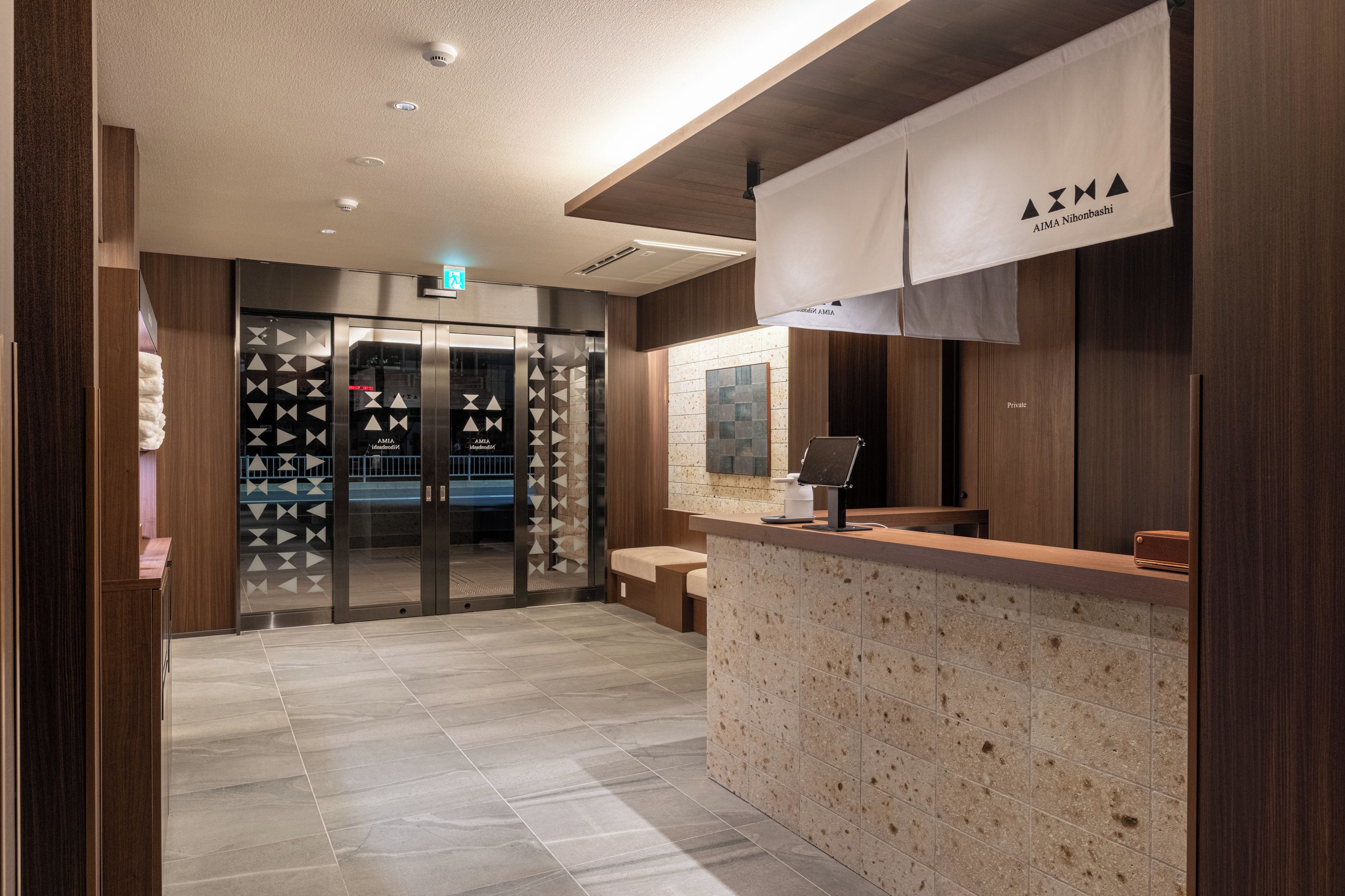 A hotel reception area with a reception desk, a seating area, and a glass elevator.
