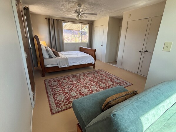 Un dormitorio con cama, ventilador de techo, ventana con cortinas, armario y sofá.