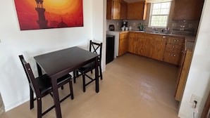 Un comedor con mesa y sillas, una cocina con armarios de madera y una ventana, y un cuadro en la pared.