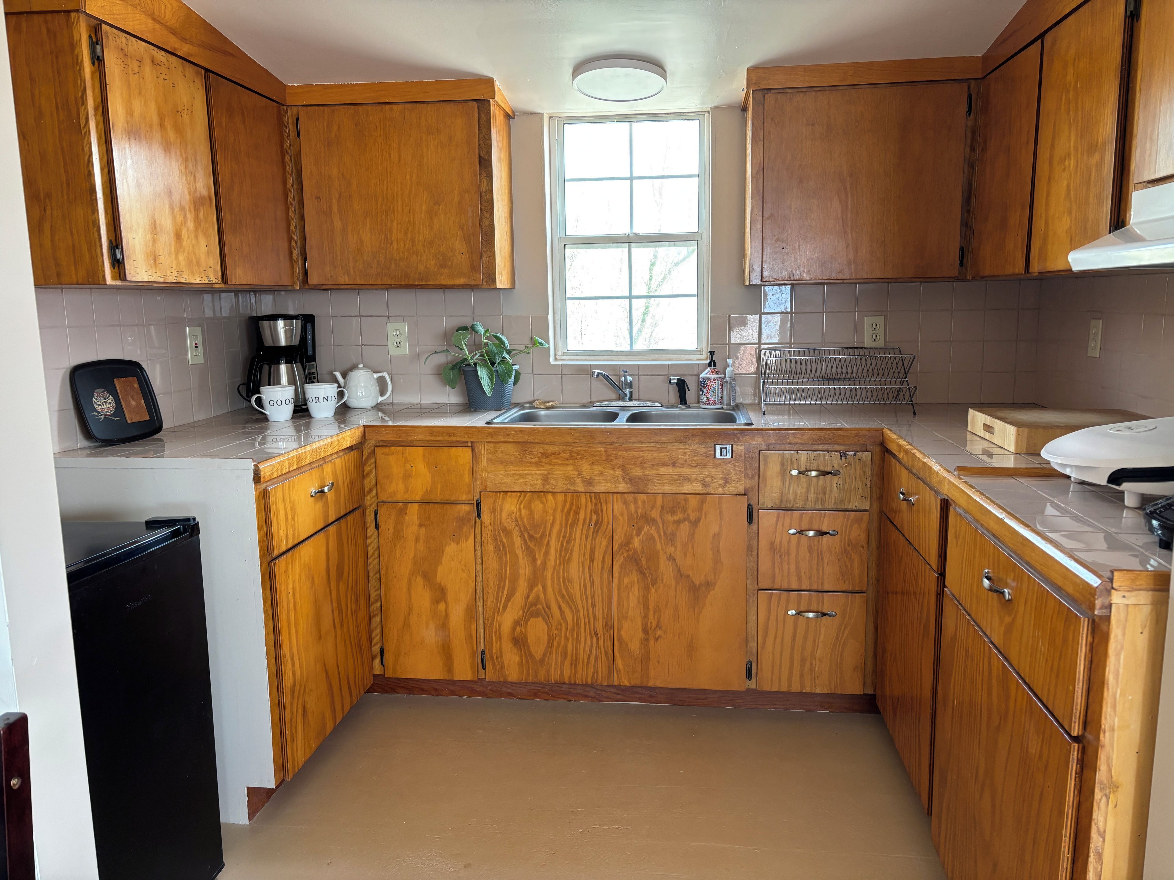 Una cocina con gabinetes de madera, un fregadero, una cafetera y un tostador.