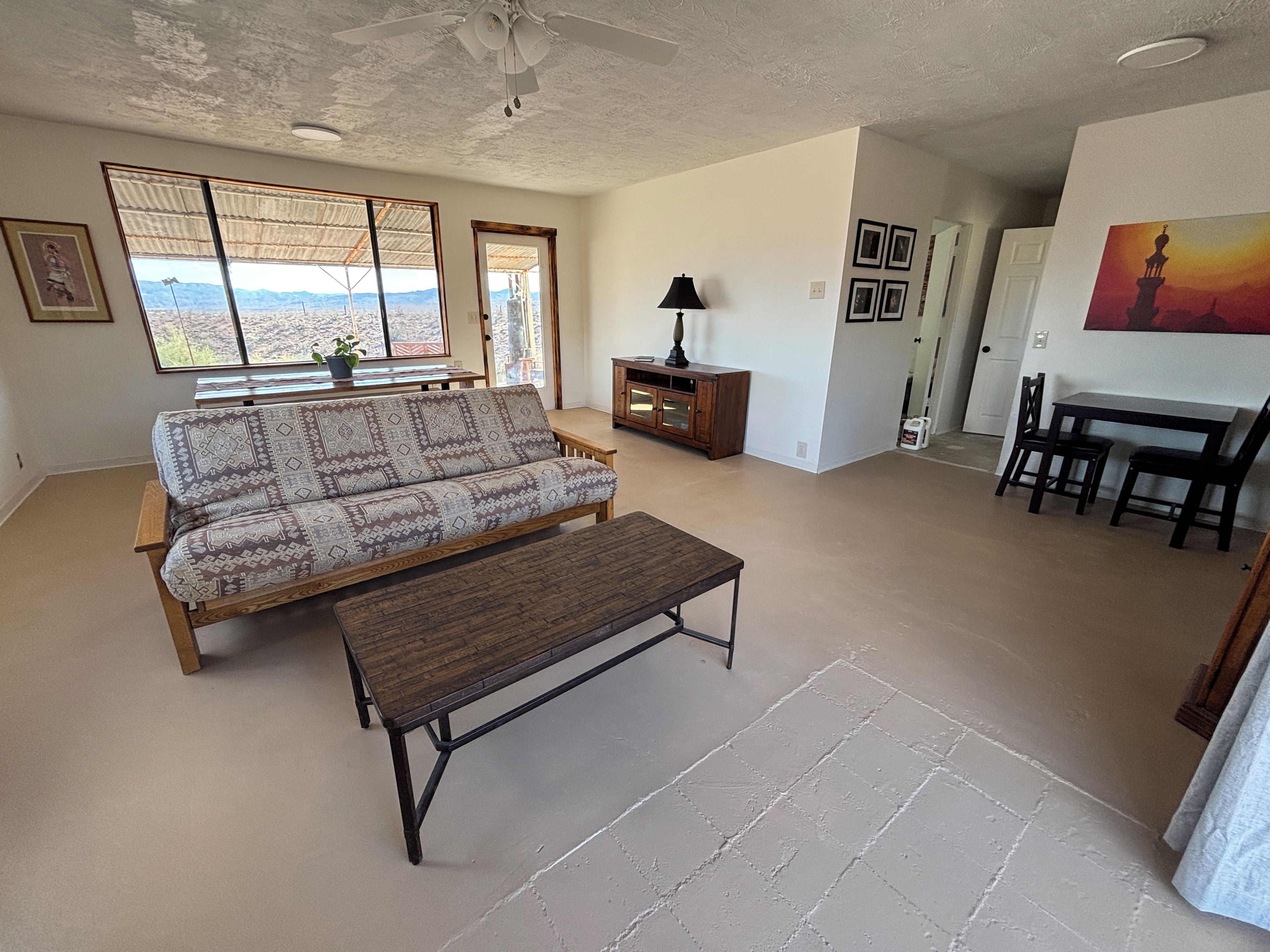 Un salon comprenant un canapé, une table basse, une table à manger avec des chaises, un ventilateur de plafond et une vue par la fenêtre.