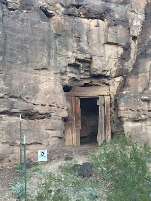A cave entrance with a wooden door, surrounded by rocky terrain and sparse vegetation. - Remote Alamo Lake Getaway!  Dark night skies. AZPT. Fishing. Farm. Ghost town. (Yucca)