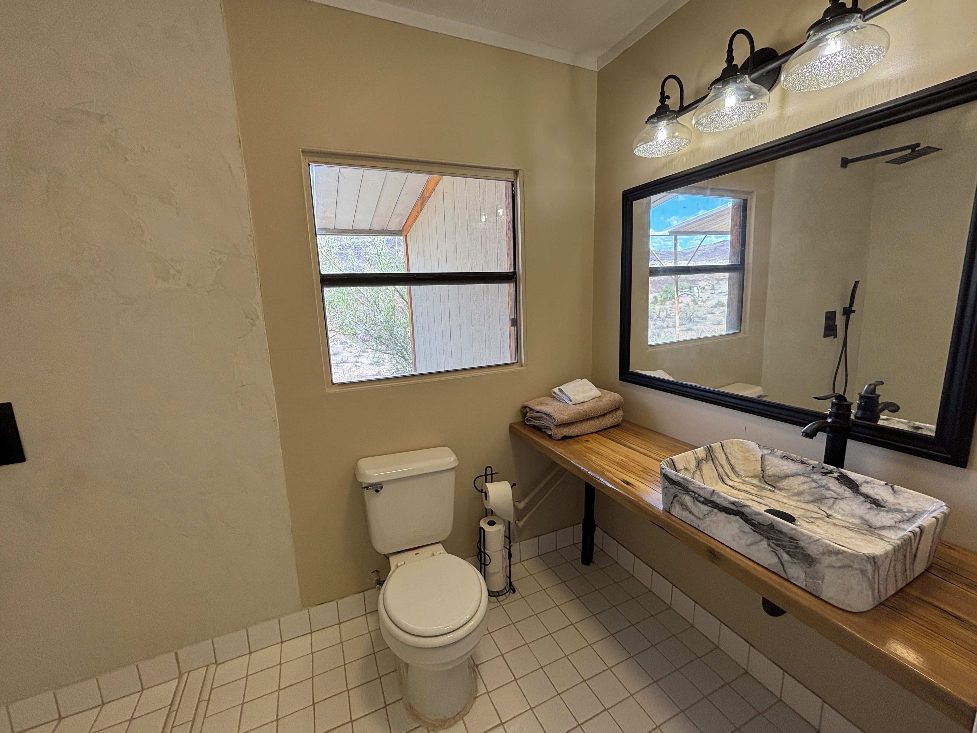 Une salle de bain avec des toilettes, un lavabo, un miroir et une fenêtre.