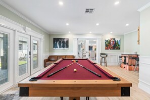 Une table de billard dans une pièce donnant sur l’extérieur, un coin repas et un bar.