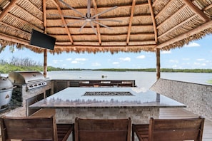 An outdoor kitchen with a stone countertop, a grill, and a ceiling fan. - Waterfront 4BR + deep water+ 2 Docks + Outdoor Kitchen, Sleeps 11 (Ruskin)