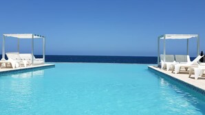 En klarblå pool med vita solstolar och parasoller, med utsikt över havet.