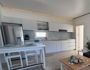 A modern kitchen with white cabinetry, a stainless steel refrigerator, and a small dining area with a table and chairs. - New stylish,1 BR, Resort access, SOV - Sea-Esta (Sosua)