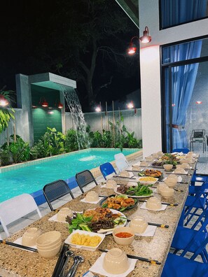 An outdoor dining area with a pool, tables set for a meal, and a waterfall feature.