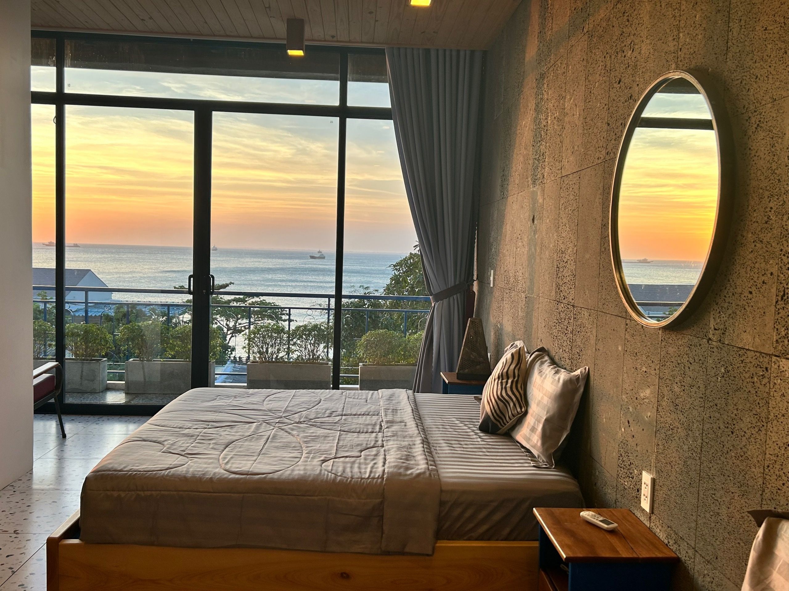 Quarto com uma grande janela, uma cama, mesa de cabeceira e espelho.