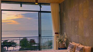 A bedroom with a large bed, a view of the sea, and a balcony with a railing.