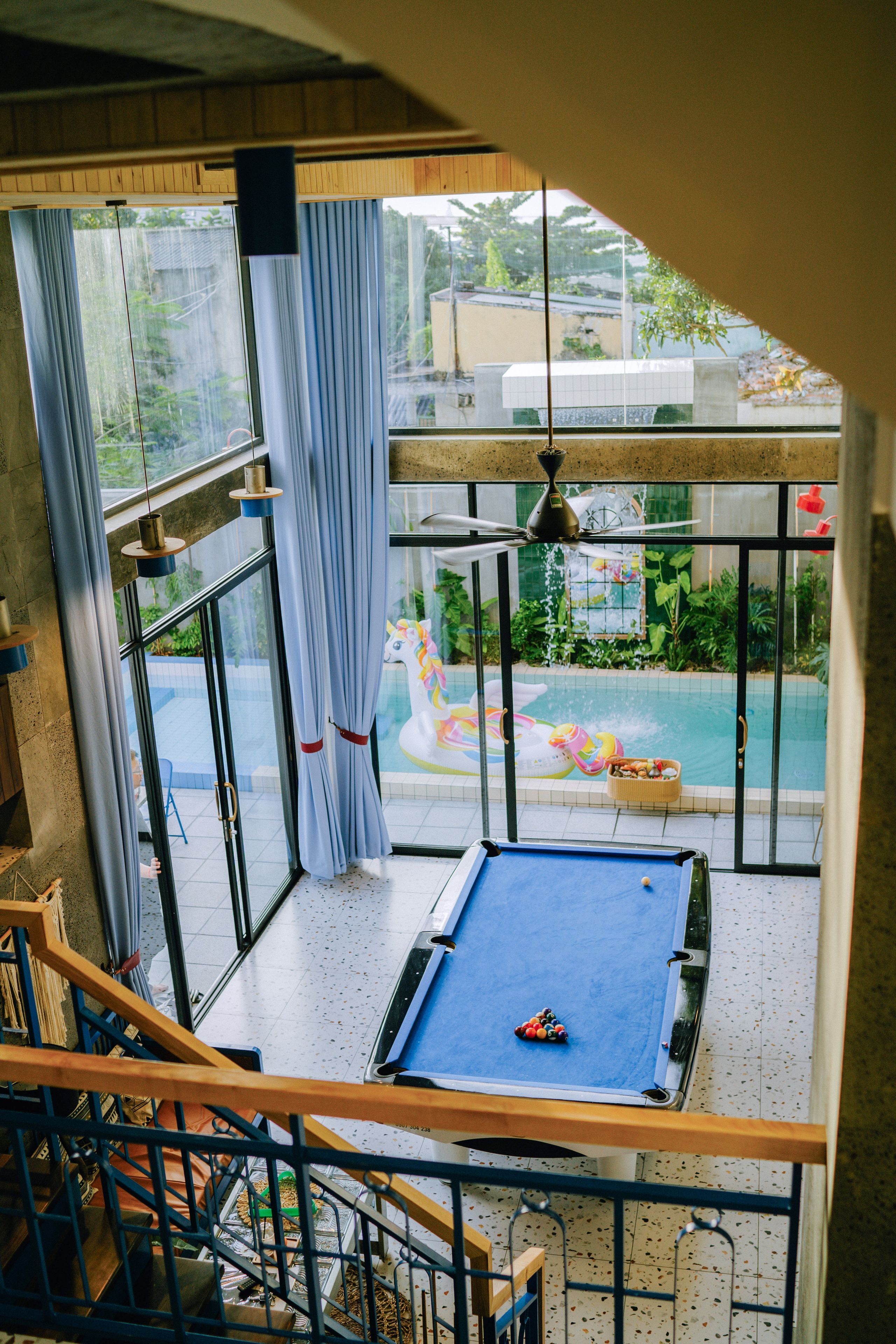 Un tavolo da biliardo in una stanza con ampie finestre, una ventola a soffitto e vista su una piscina esterna.