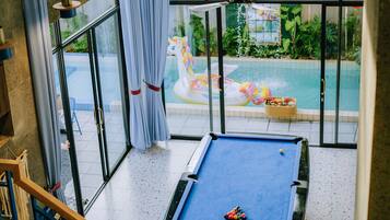 Un tavolo da biliardo in una stanza con ampie finestre, una ventola a soffitto e vista su una piscina esterna.