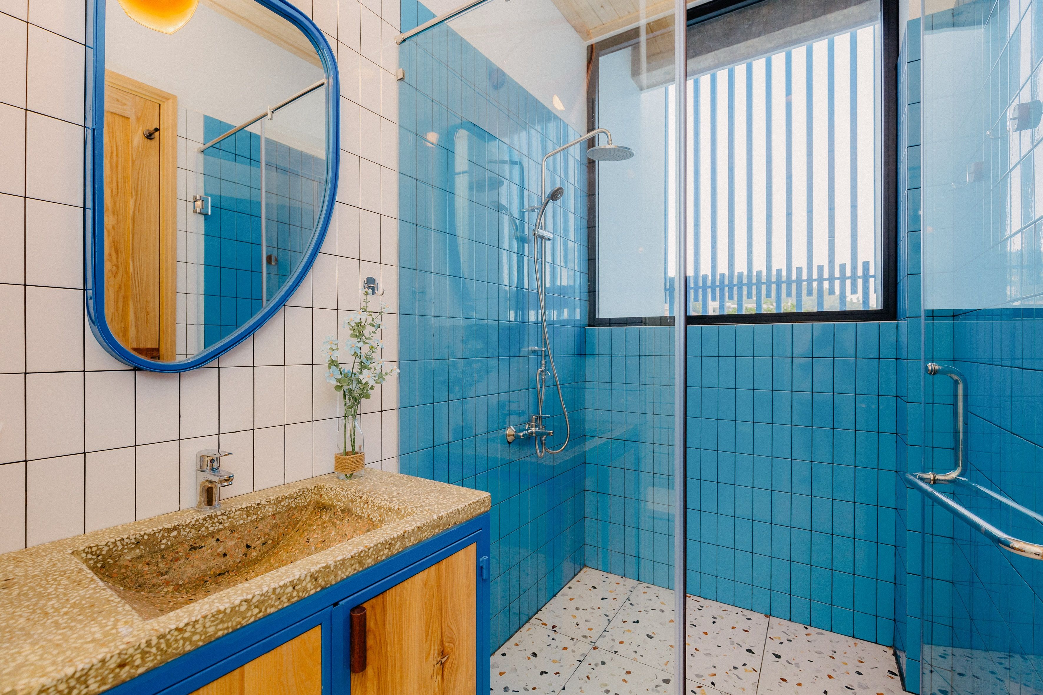 Ein Badezimmer mit blauen Fliesen, einem Holzkosmetikschrank und einem Waschbecken sowie einer Glasdusche.