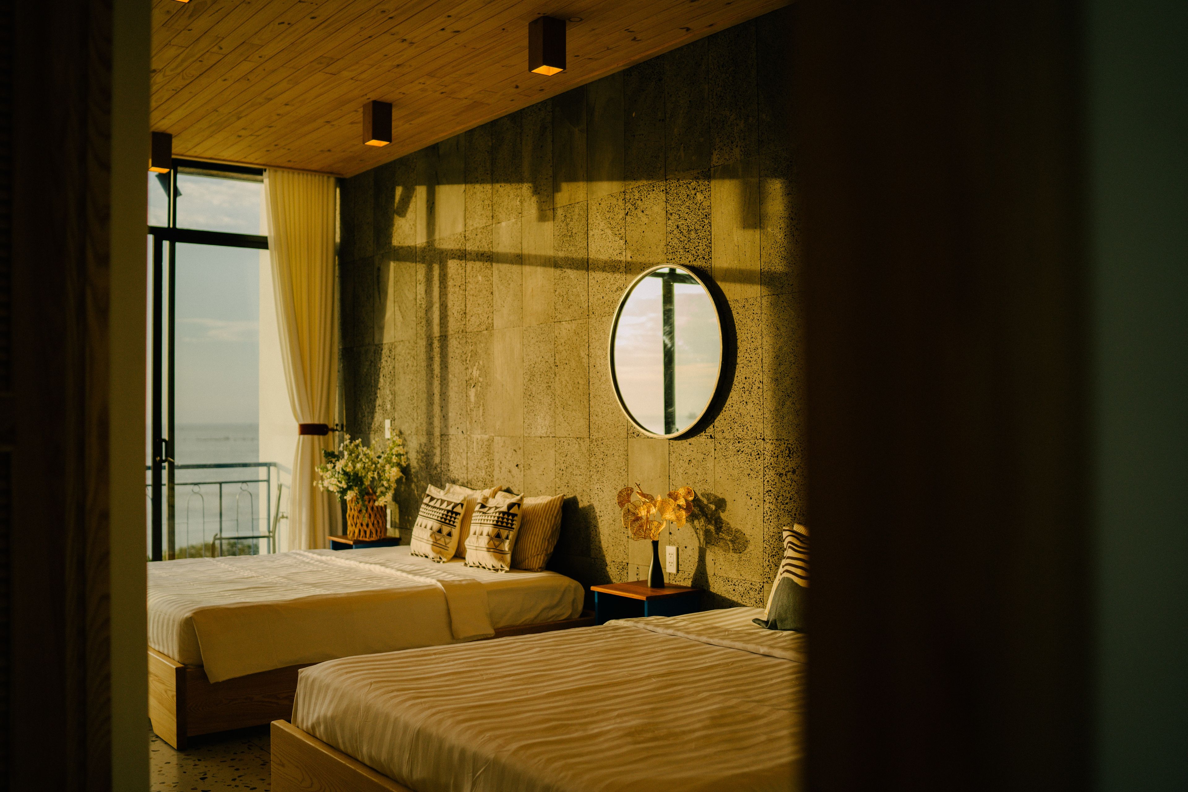 A hotel room with two beds, a large mirror, and a view of the sea through a window.
