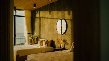 A hotel room with two beds, a large mirror, and a view of the sea through a window.