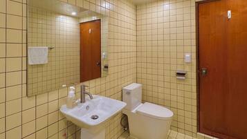 A bathroom with a sink, toilet, and mirror. There are slippers on the floor.