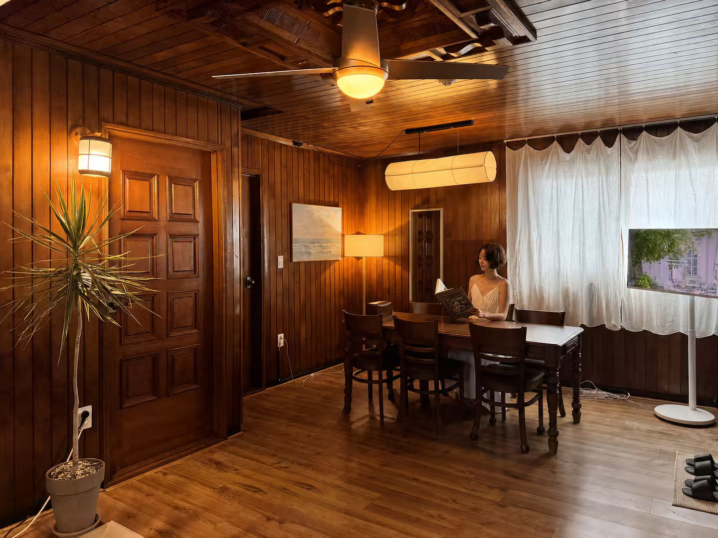 A wooden-paneled room with a dining table, chairs, a potted plant, and a ceiling fan.