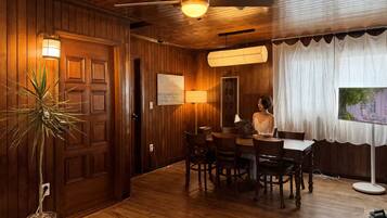 A wooden-paneled room with a dining table, chairs, a potted plant, and a ceiling fan.