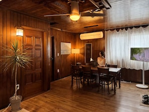 Una habitación con paneles de madera, una mesa de comedor, sillas, una planta en maceta y un ventilador de techo.