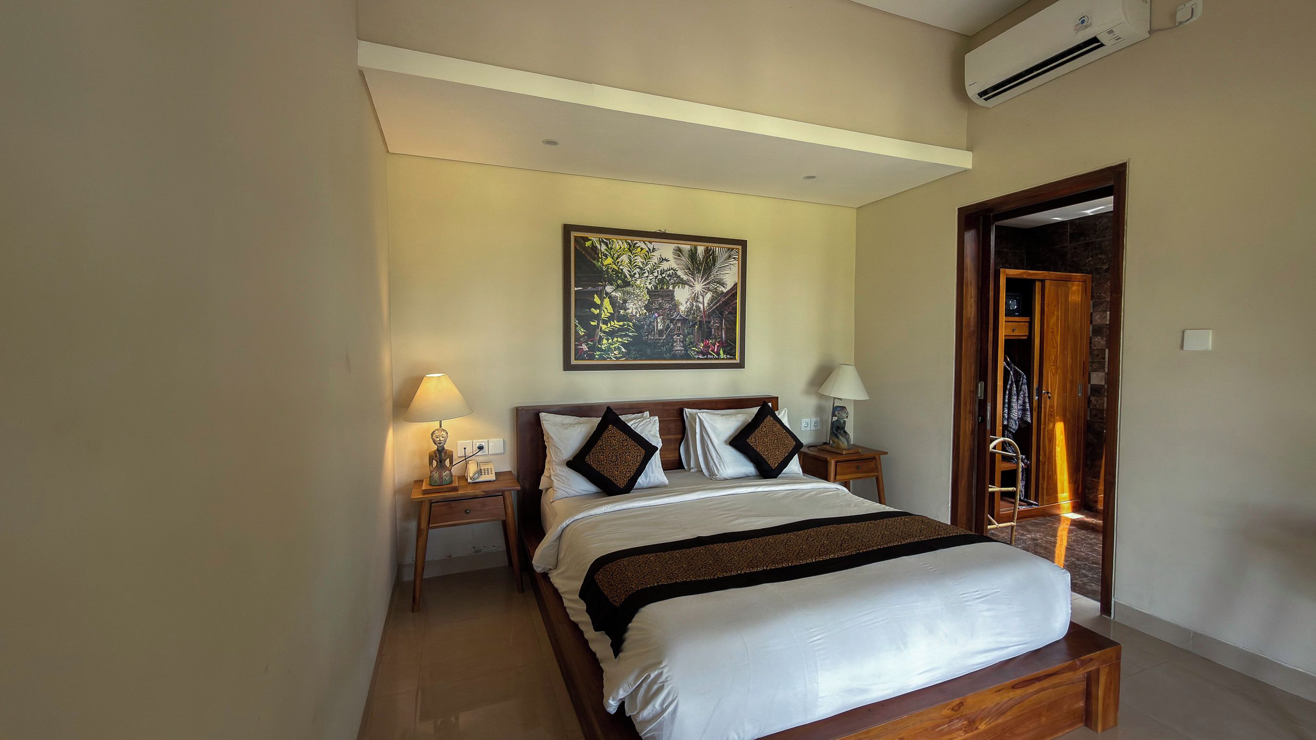 Habitación de hotel con una cama, dos mesitas de noche, aire acondicionado en la pared y una puerta que da a otra habitación.