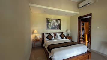 Habitación de hotel con una cama, dos mesitas de noche, aire acondicionado en la pared y una puerta que da a otra habitación.