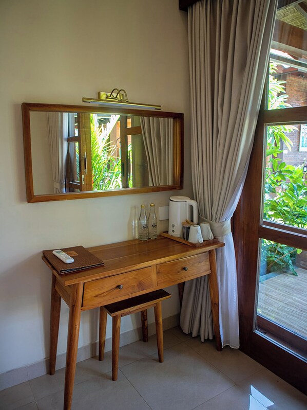 A wooden desk with a mirror, a remote control, and a tray with bottles and a coffee maker.