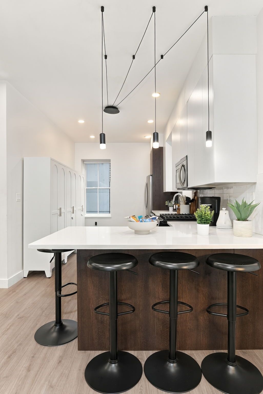 A modern kitchen with a central island, bar stools, pendant lighting, and white cabinetry.