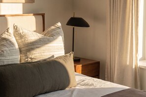 Un lit bien fait, avec des oreillers, une lampe de chevet et une table de chevet en bois.