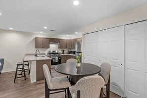 Une cuisine moderne avec un îlot central, un coin repas avec une table ronde et des chaises, et une porte blanche sur le côté droit.