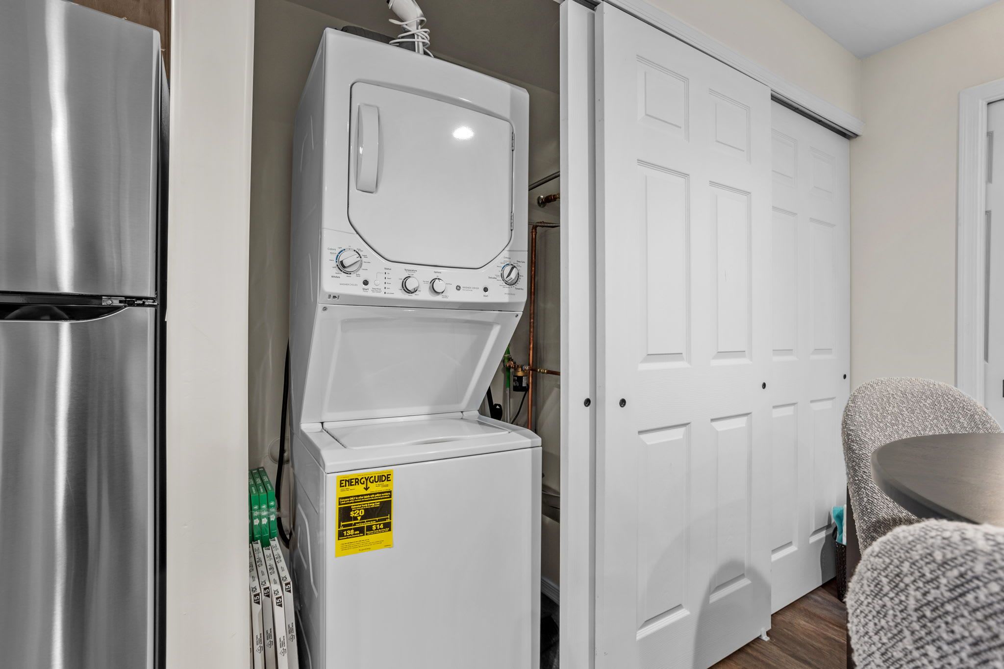 A compact kitchen with a stainless steel refrigerator, a white washing machine, and a white wardrobe with a sliding door.