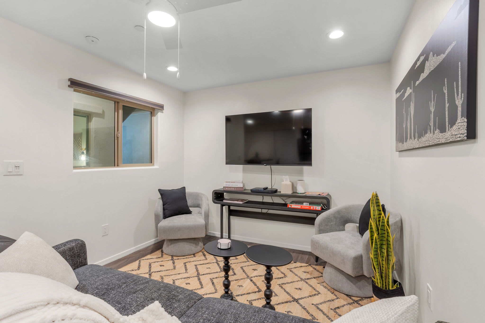 A modern living room with a flat-screen TV, two grey armchairs, a sofa, a coffee table, and a decorative plant.